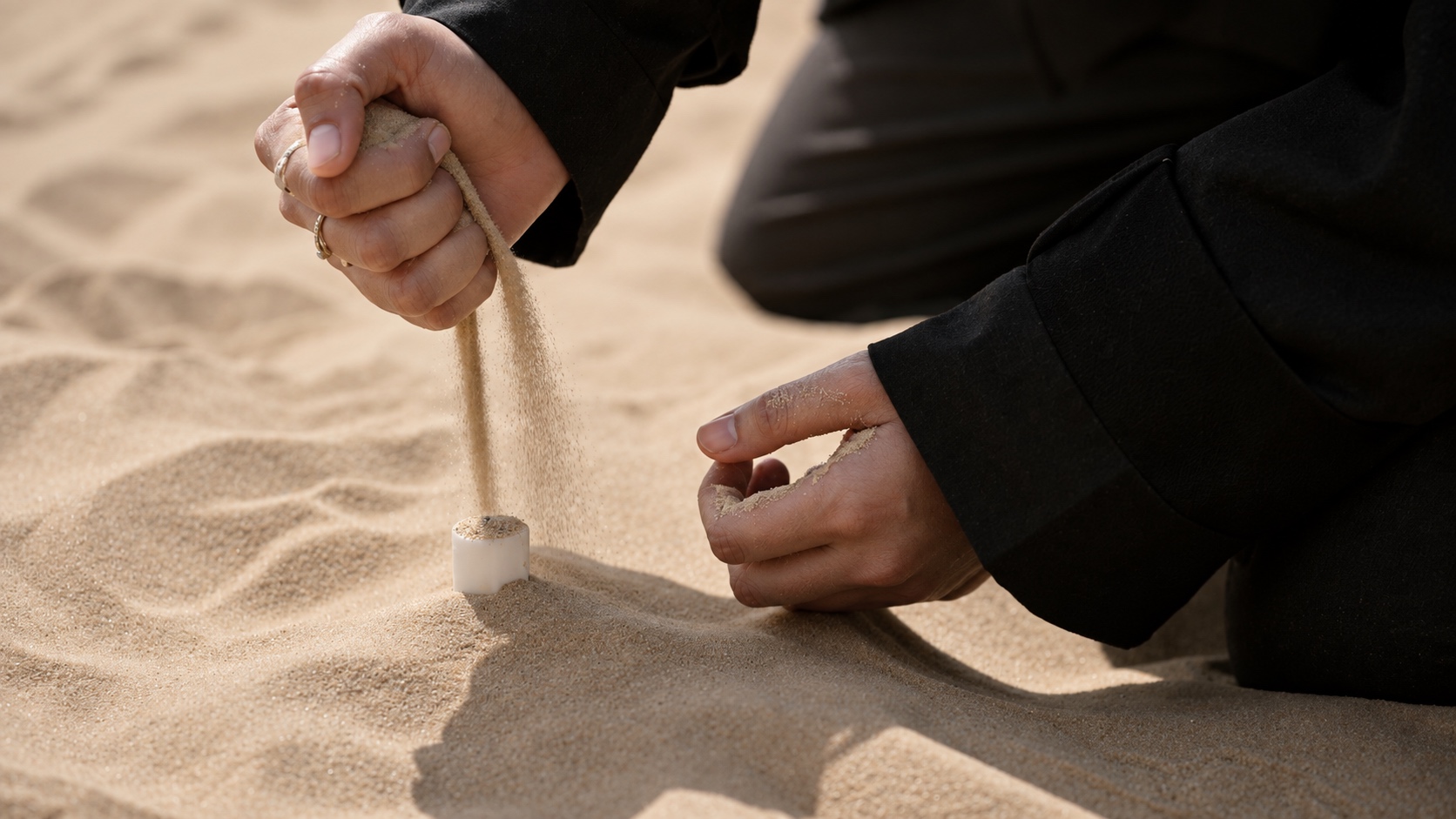 Sand slips through a hand onto a candle buried in the dune