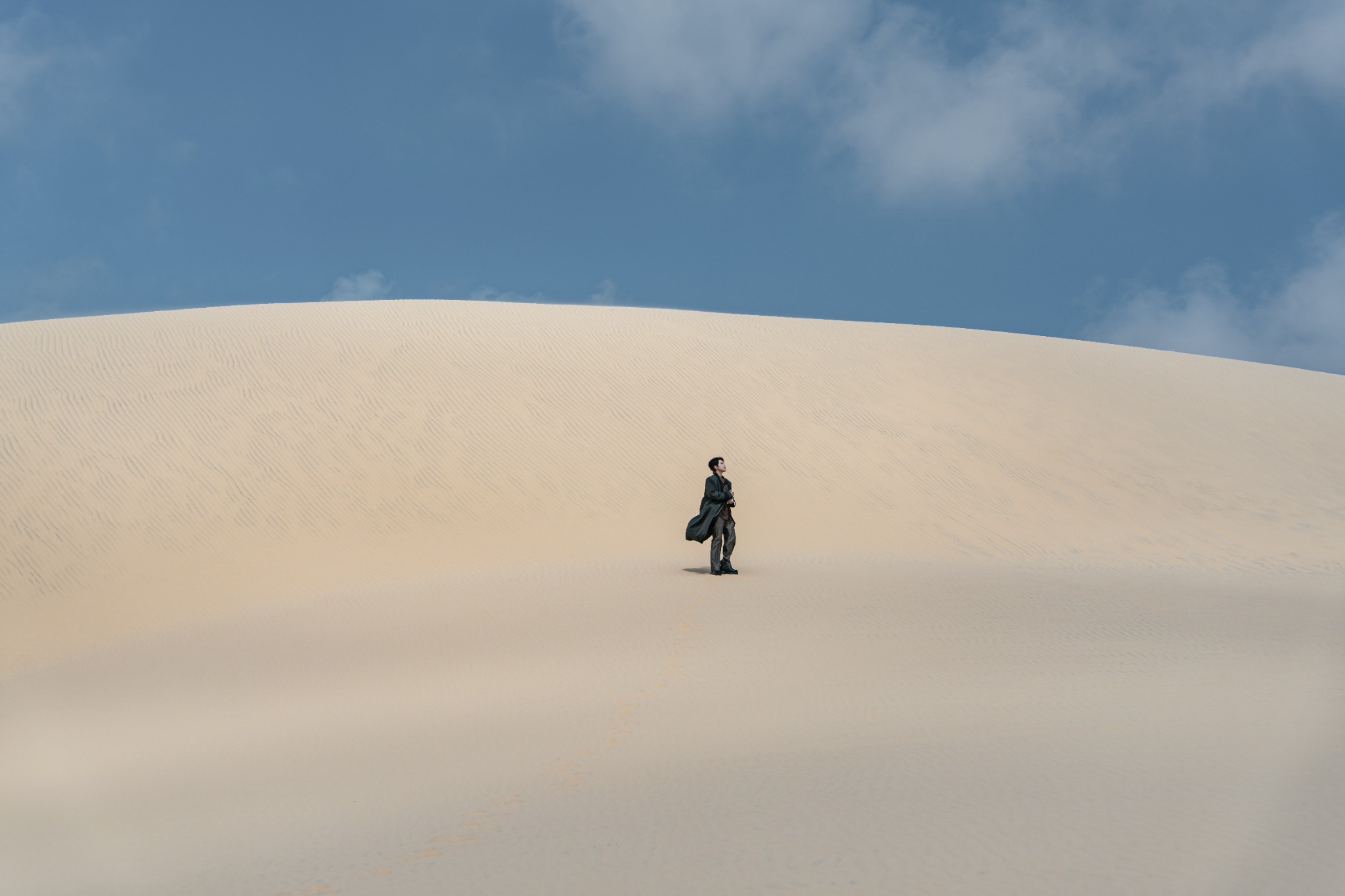 A small figure walking across the vast dune